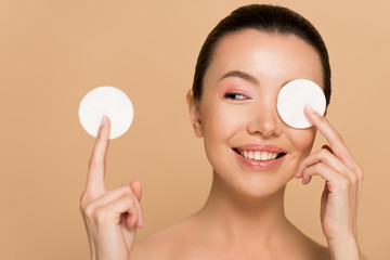 happy naked asian girl removing makeup from face with cotton pads isolated on beige © LIGHTFIELD STUDIOS