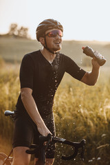 Strong bearded man in active wear, protective helmet and sport glasses splashing fresh water from...