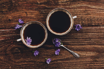 Lilac chicory flowers, cups and spoon on wooden table.
