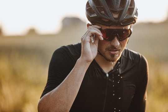 Portrait of bearded man in black helmet and mirrored eyewear feeling tired because of hard training. Mature cyclist with wet face taking break during workout.