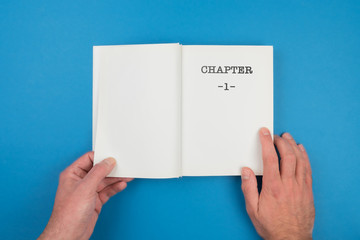 top view of person fiipping open a book with text CHAPTER 1 on first page against blue background