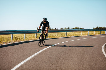 Active mature man in sport outfit riding bicycle on paved road in countryside. Experienced cyclist...