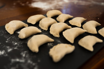 Uncooked russian vareniki on cutting wooden board with flour on baking paper. Process of making vareniki. top view.Typical Eastern European food, called dumplings, dumplings, dumplings, pies or pies