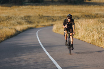 Mature sportsman in activewear, protective helmet and sunglasses riding bike and holding bottle...