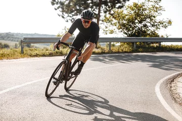  Bearded cyclist in sport clothing, protective helmet and mirrored glasses riding black bike among countryside nature during summer time. Mature man preparing for competitions and races. © Tymoshchuk