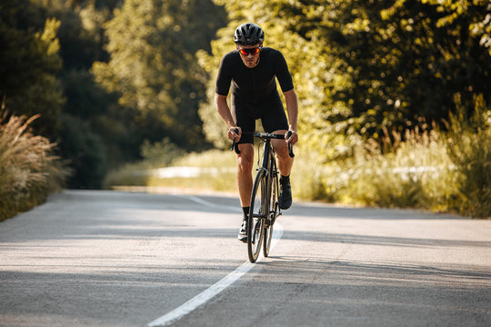 Strong sportsman with athletic body wearing black sport clothing, helmet and sunglasses practicing in cycling on fresh air. Concept of healthy hobby and regular trainings
