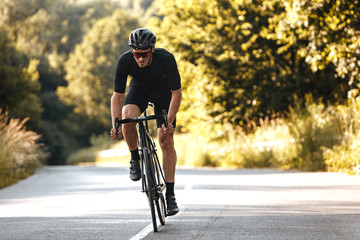 Full length portrait of active man in sport clothing and protective helmet riding bike with blur background of summer nature. Concept of workout and races.