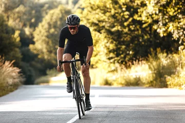 Tuinposter Full length portrait of active man in sport clothing and protective helmet riding bike with blur background of summer nature. Concept of workout and races. © Tymoshchuk