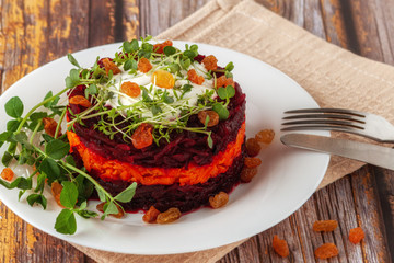 A healthy detox salad with beets, carrots, microgreen and raisins. Vegetarian vegan food on a wooden background.
