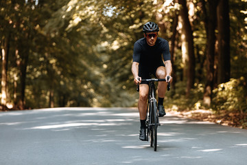 Fototapeta na wymiar Mature bearded man in active wear and protective helmet dynamically riding bike on paved road. Bicyclist in mirrored eyeglasses enjoying favore hobby on fresh air.