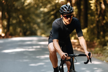 Mature man with athletic body in sport outfit, protective helmet and mirrored glaases riding bike...
