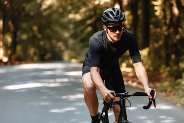 Foto op Canvas Mature man with athletic body in sport outfit, protective helmet and mirrored glaases riding bike among summer forest. Bearded male practising in cycling on fresh air. © Tymoshchuk