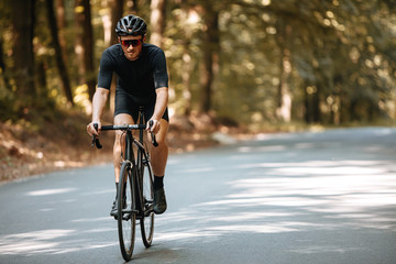 Mature man in sport clothing, protective helmet and sunglasses riding black professional bike with...
