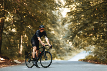 Mature athlete with sporty body shape dressed in cycling clothing, helmet and eyeglasses standing with bike in summer forest. Bearded man enjoying fresh air during sport activity.