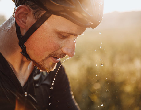 Close up portrait of tired bearded athlete in protective helmet with water drops on his face. Mature man splashed water to refresh after hard training.