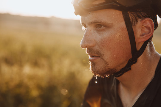 Portrait of bearded man in black helmet feeling tired because of riding bike outdoors. Strong cyclist with drops of sweat on his face  having break during training.