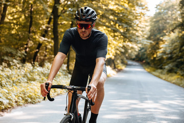 Bearded man with athletic body shape wearing sport clothing and mirrored glasses, riding bicycle...