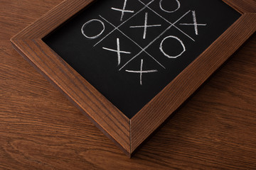 tic tac toe game on blackboard with chalk grid, naughts and crosses on wooden surface