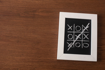 top view of tic tac toe game on blackboard with crossed out row of crosses on wooden surface