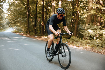 Fototapeta na wymiar Active bearded man in sport clothing and black helmet riding bicycle with beautiful nature around. Mature cyclist in mirrored glasses doing favorite hobby outdoors.