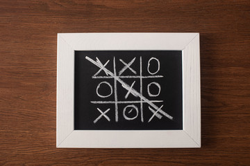 top view of tic tac toe game on blackboard with crossed out row of crosses on wooden surface