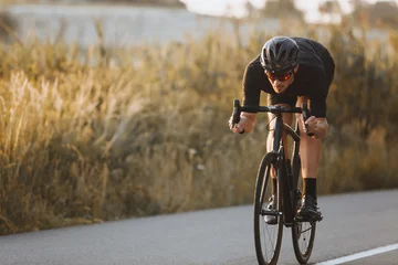 Foto op Plexiglas Active professional sportsman cyclist wearing black sports outfit, helmet and glasses riding bike at the paved road outdoors. Strong man improving skills and getting ready for cycling competition © Tymoshchuk