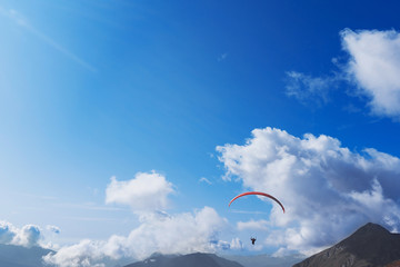 Paraglider flying over the mountains on a bright summer day. Paragliding sport concept. Copy space.