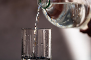 Pouring water from plastic bottle into a glass on blurred background. Selective focus and copy space