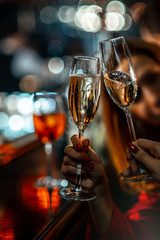 The girls at the bar clink glasses with sparkling wine. Clinking champagne glasses with friends. The atmosphere of a night club. Close-up of hands