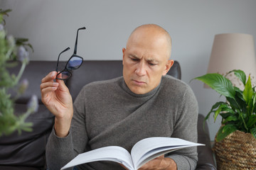 A man sits on a sofa with a book thinking. Book and phone in our life.