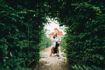 A young caucasian stylish couple hugging in arch with greenery on a red palace background