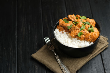 Chicken tikka masala traditional Asian spicy meat food with rice tomatoes and cilantro in a black bowl on dark background.