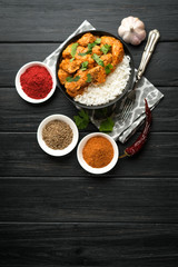 Chicken tikka masala traditional Asian spicy meat food with rice tomatoes and cilantro in a black bowl on dark background.