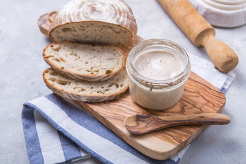 Fresh homemade bubbly sourdough starter, a fermented mixture of water and flour to use as leaven for bread baking, on wooden table