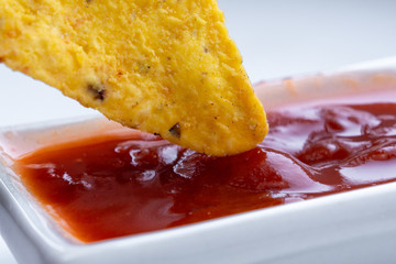 Delicious mexican nachos chips and tomato sauce, close-up. Corn tortilla chips, dunked in the sauce