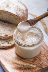 Fresh homemade bubbly sourdough starter, a fermented mixture of water and flour to use as leaven for bread baking, on wooden table