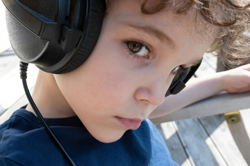 Portrait of six-year-old boy listening music with big headphones.