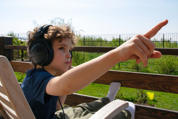 A six-year-old boy with big headphones pointing his finger at at something.