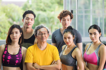 A group of fitness players of a variety of age groups, including the elderly, middle-aged and young people, both women and men They wear exercise clothes, standing in the gym.