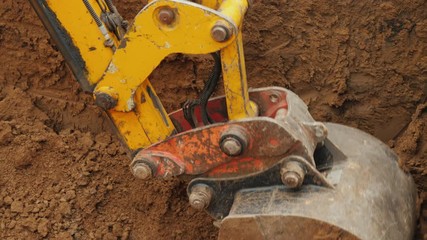 Earthmoving equipment at a construction site. Excavator bucket removes ground from trench
