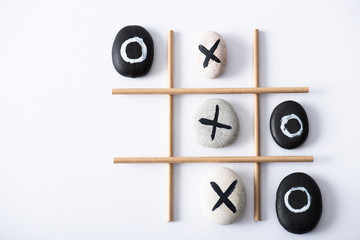 top view of tic tac toe game with grid made of paper tubes, and pebbles marked with crosses and naughts on white surface