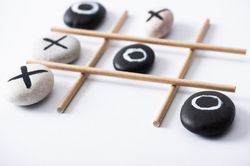 selective focus of tic tac toe game with grid made of paper tubes, and pebbles marked with naughts and crosses on white surface