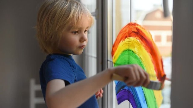 Little boy drawing rainbow on  window while coronavirus quarantine. Rainbow sign is symbol of hope, means that everything will be OK. Stay at home for lockdown coronavirus.