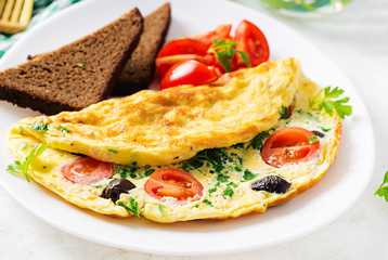 Breakfast. Omelette with tomatoes, black olives, cottage cheese and green herbs on white plate.  Frittata - italian omelet.