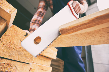 The carpenter is cutting the wooden plank by the saw