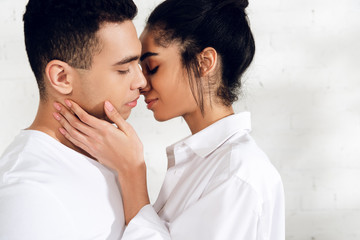 African american woman with closed eyes kissing man on white background