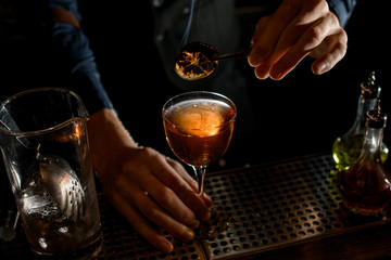 Close-up. Bartender holds tweezers with slice of citrus over glass of drink.