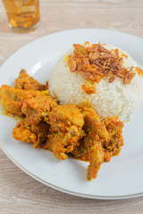Nasi ayam rica-rica in white plate. Indonesian food made from chicken and various seasonings. has a spicy taste. wooden background