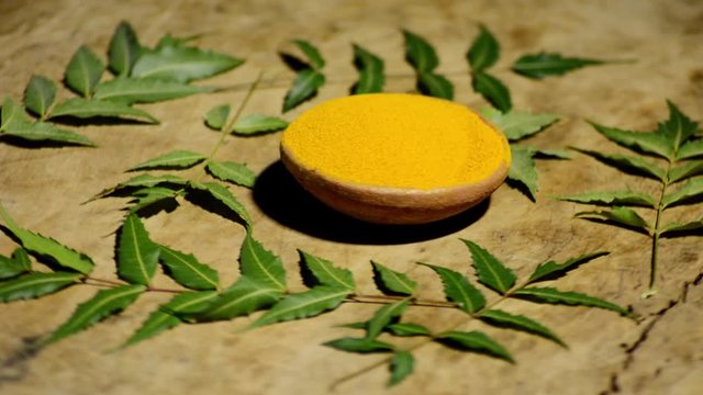Medicinal turmeric powder with neem leaves over wood background