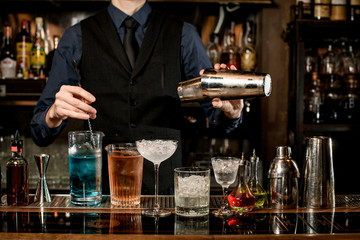 professional bartender holds steel shaker and mixes cocktail